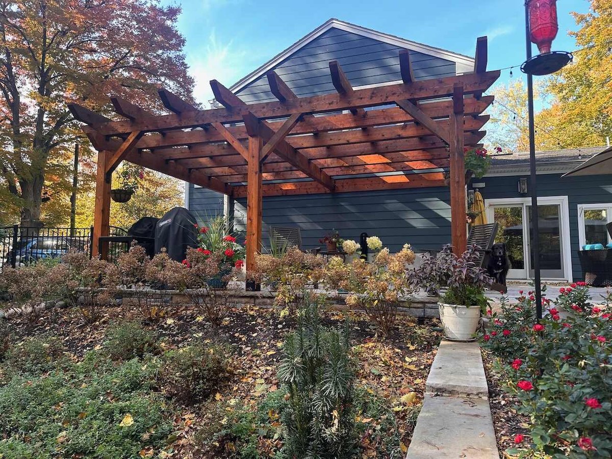 Backyard pergola with wood beams and seasonal garden plants in Ridgewood, NJ by Fairmount Heights Homes.