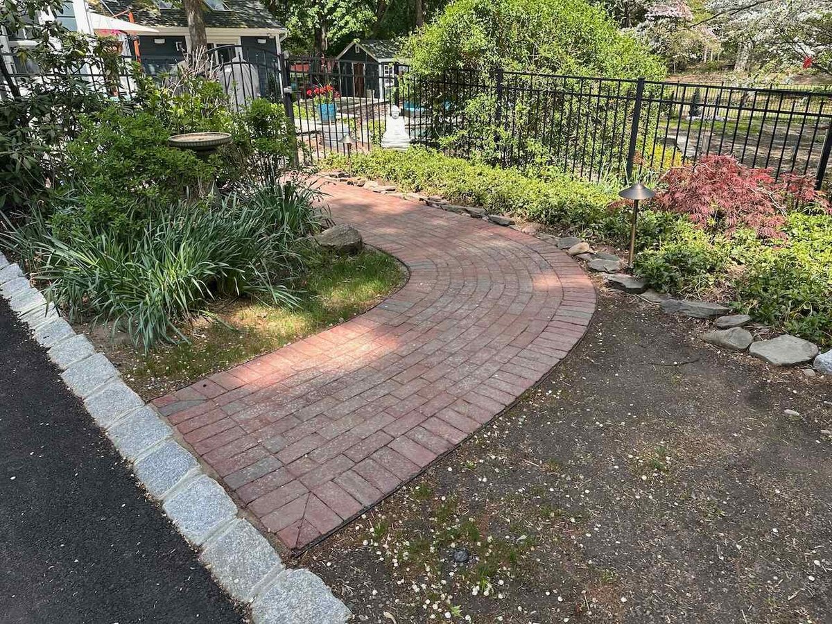 Curved red brick walkway installation surrounded by garden beds in Ridgewood, NJ by Fairmount Heights Homes.