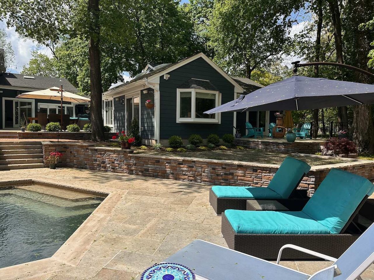 Outdoor living area with sun loungers and umbrella beside pool in Ridgewood, NJ by Fairmount Heights Homes.