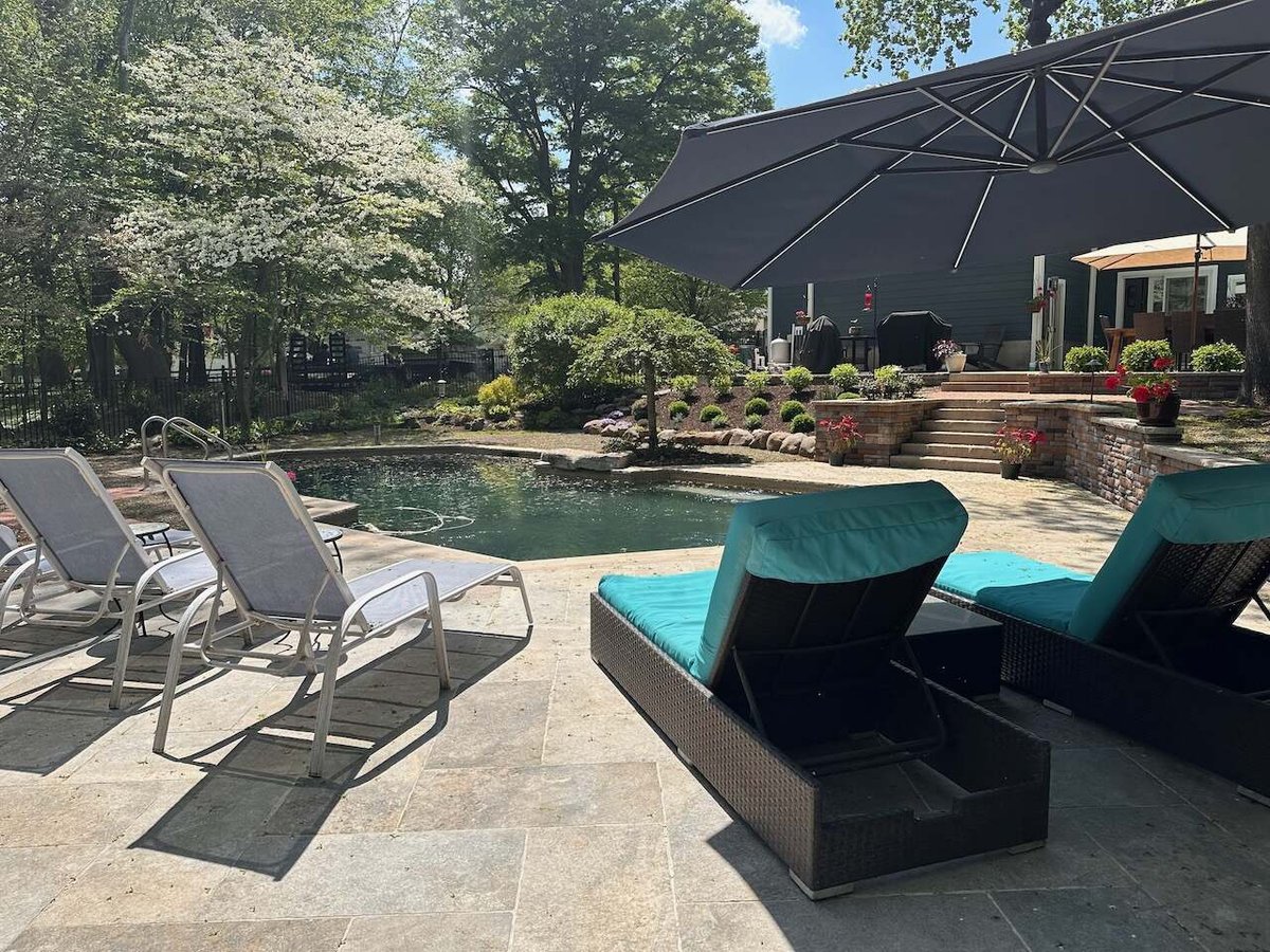 Outdoor living space with modern lounge chairs, pool, and umbrella in Ridgewood, NJ by Fairmount Heights Homes.