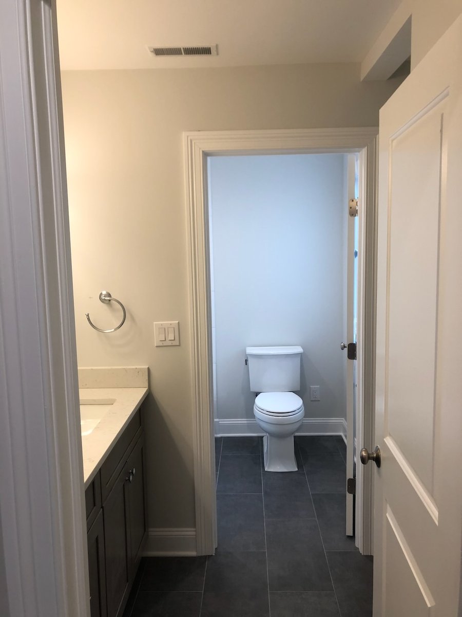 Hallway bathroom with dark floor tile and view of toilet in Ridgewood custom home by Fairmount Heights Homes.