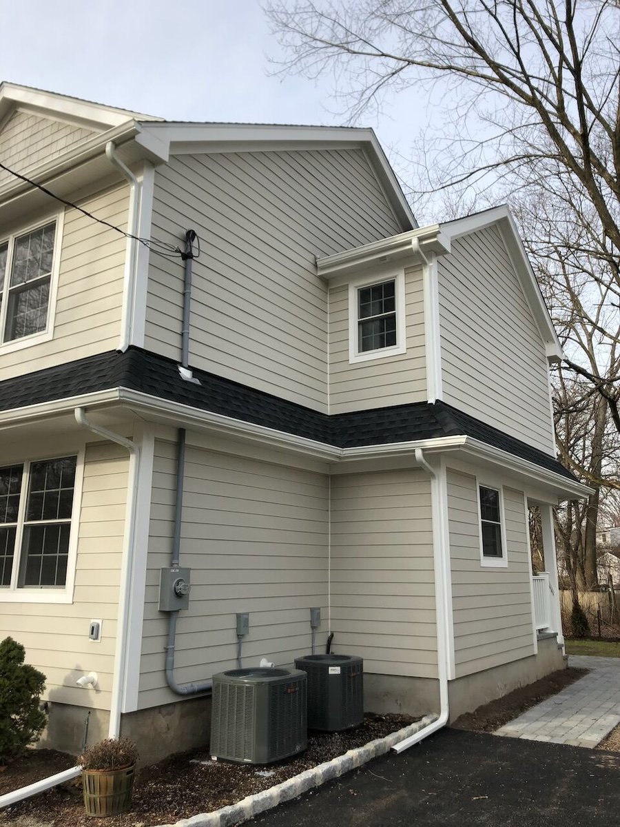 Rear corner view of a beige custom home in Ridgewood, NJ by Fairmount Heights Homes showing HVAC units.