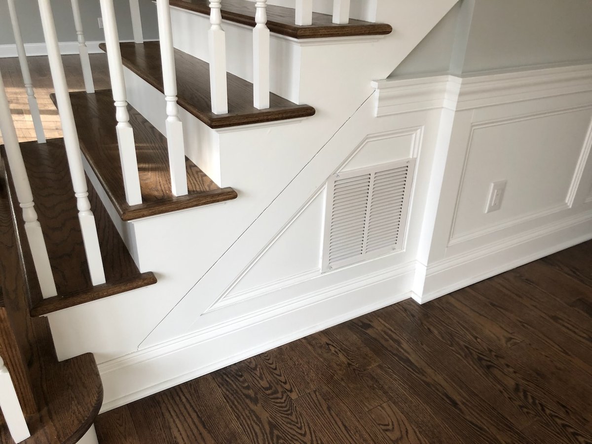 Staircase with white balusters and wood treads above decorative wall panels in Ridgewood home by Fairmount Heights Homes.