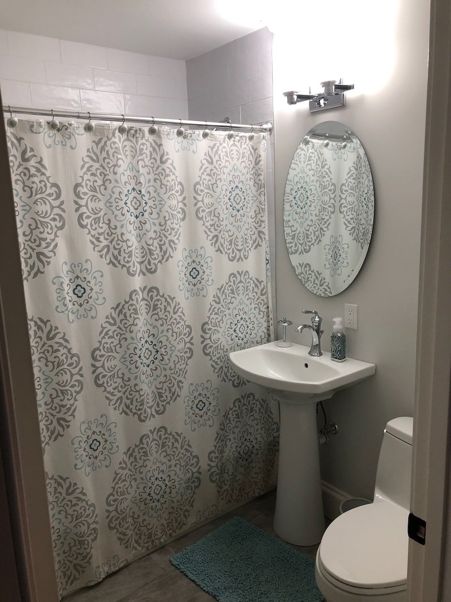 Full bathroom with patterned shower curtain and pedestal sink in Ridgewood, NJ home by Fairmount Heights Homes.