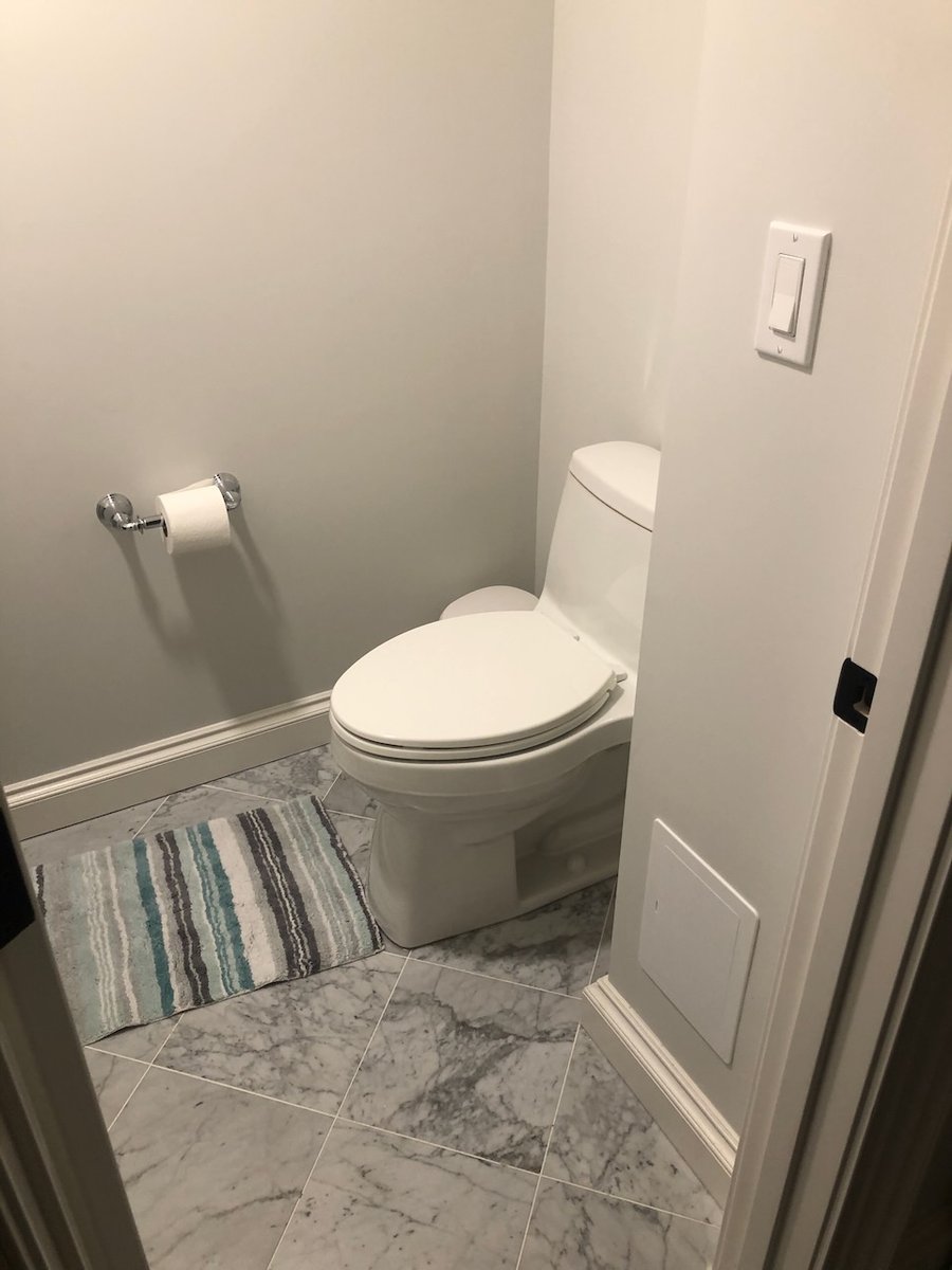 Minimalist bathroom with white toilet, striped rug, and marble tile flooring in Ridgewood, NJ by Fairmount Heights Homes.