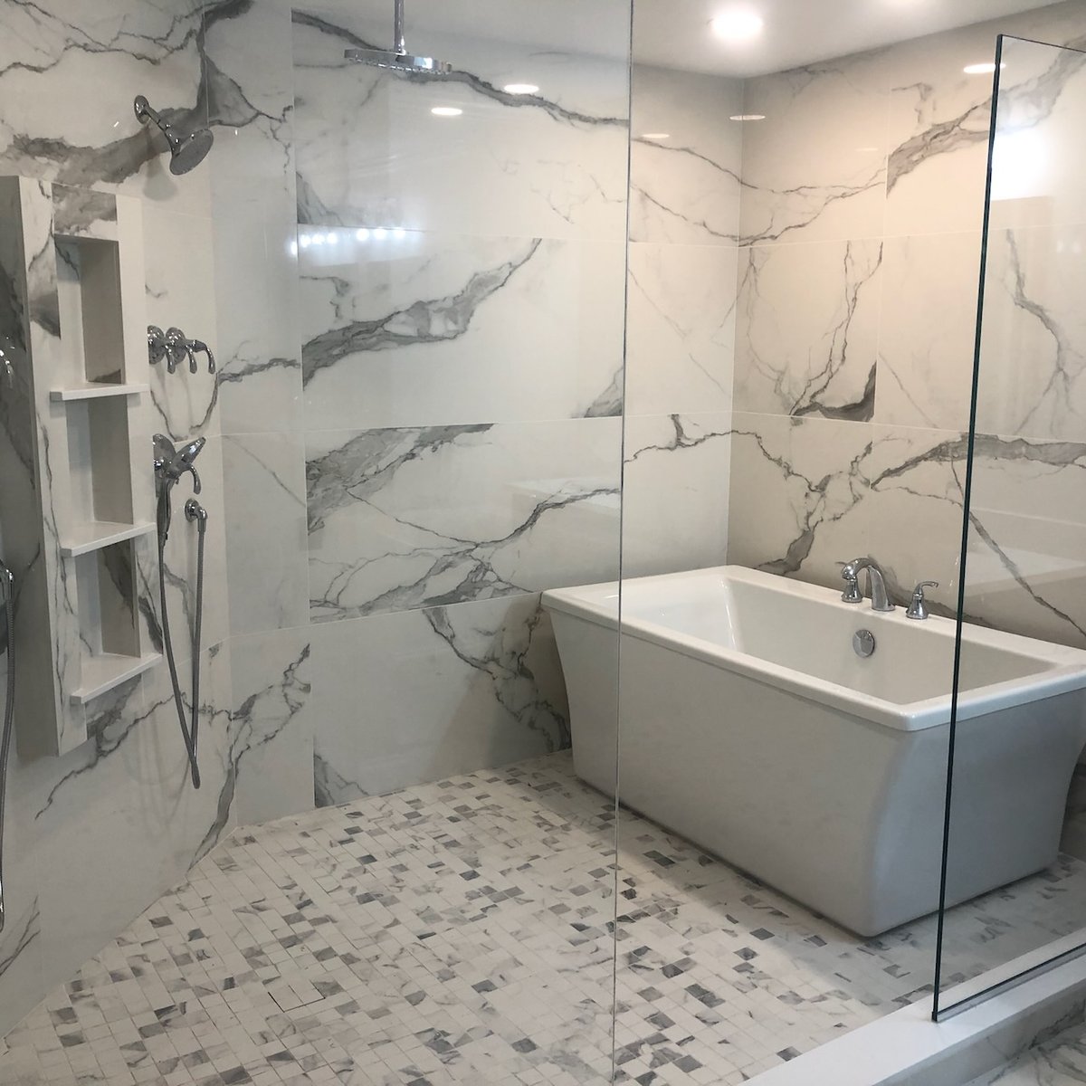 Modern glass shower and soaking tub with marble walls in Ridgewood, NJ bathroom by Fairmount Heights Homes.