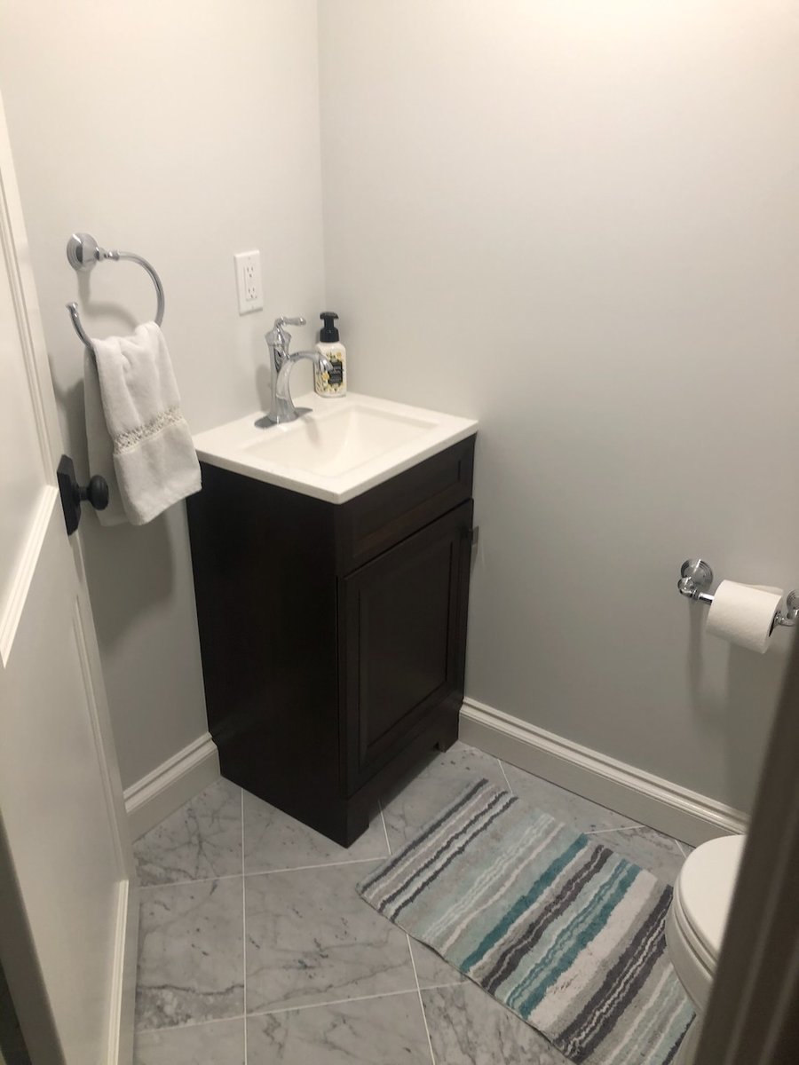 Small powder room with dark wood vanity and marble tile flooring in Ridgewood, NJ by Fairmount Heights Homes.
