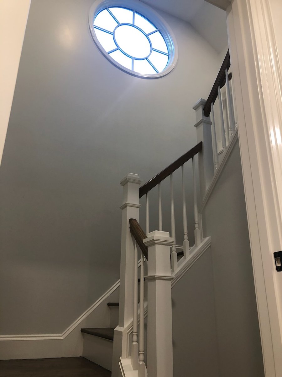 Stairwell featuring custom white railing and round accent window in Ridgewood, NJ home by Fairmount Heights Homes.