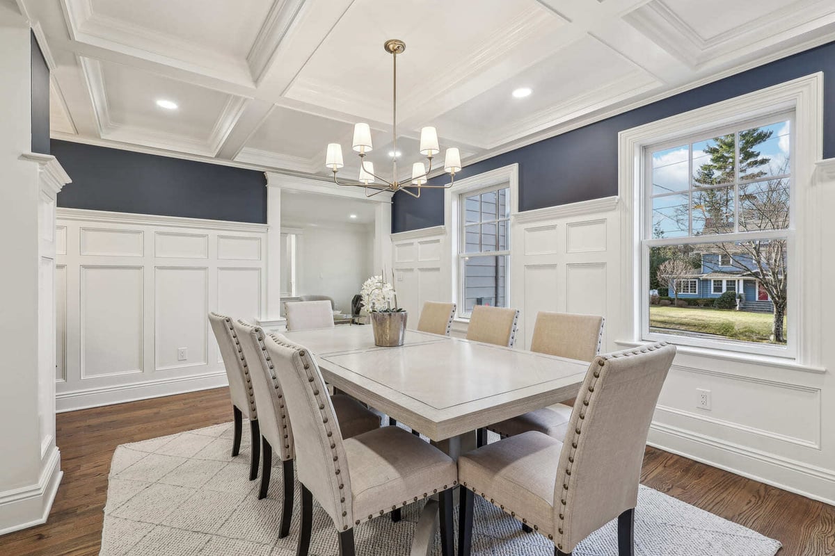Formal dining room in Ridgewood, NJ with coffered ceiling, navy walls, and upholstered chairs