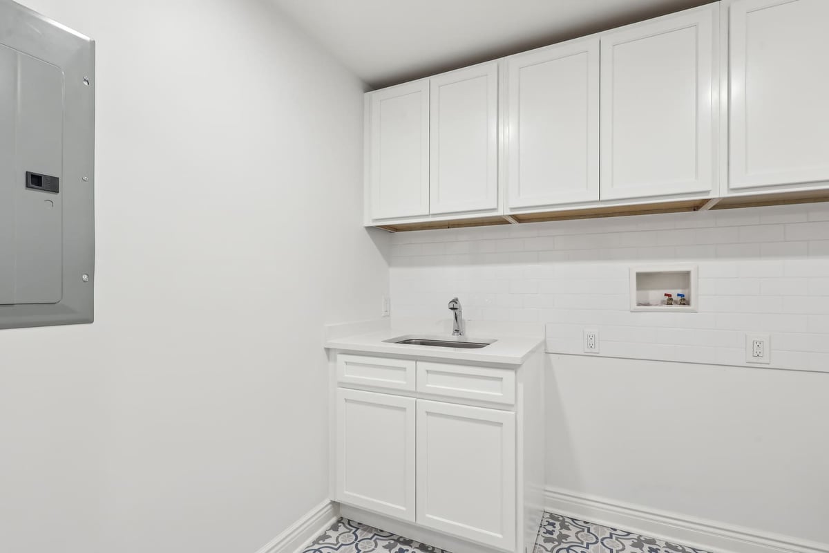 Laundry room in Ridgewood, NJ with white cabinets, utility sink, and patterned tile floor