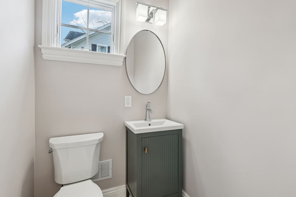 Powder room in Ridgewood, NJ with pedestal sink, oval mirror, and window