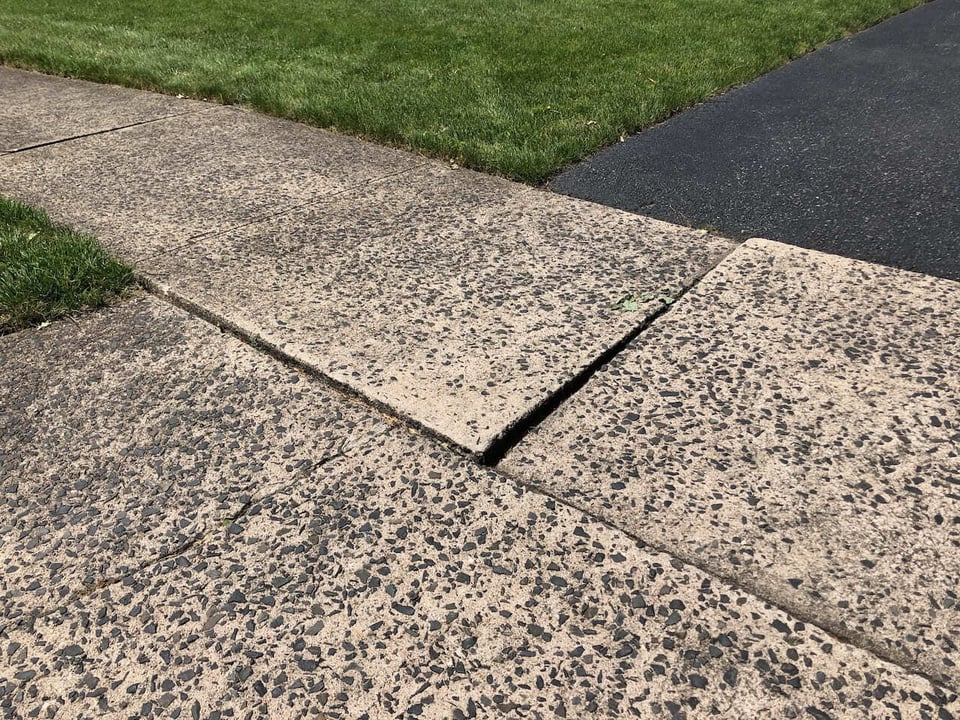 Raised concrete sidewalk slab in Ridgewood creating an uneven trip hazard.
