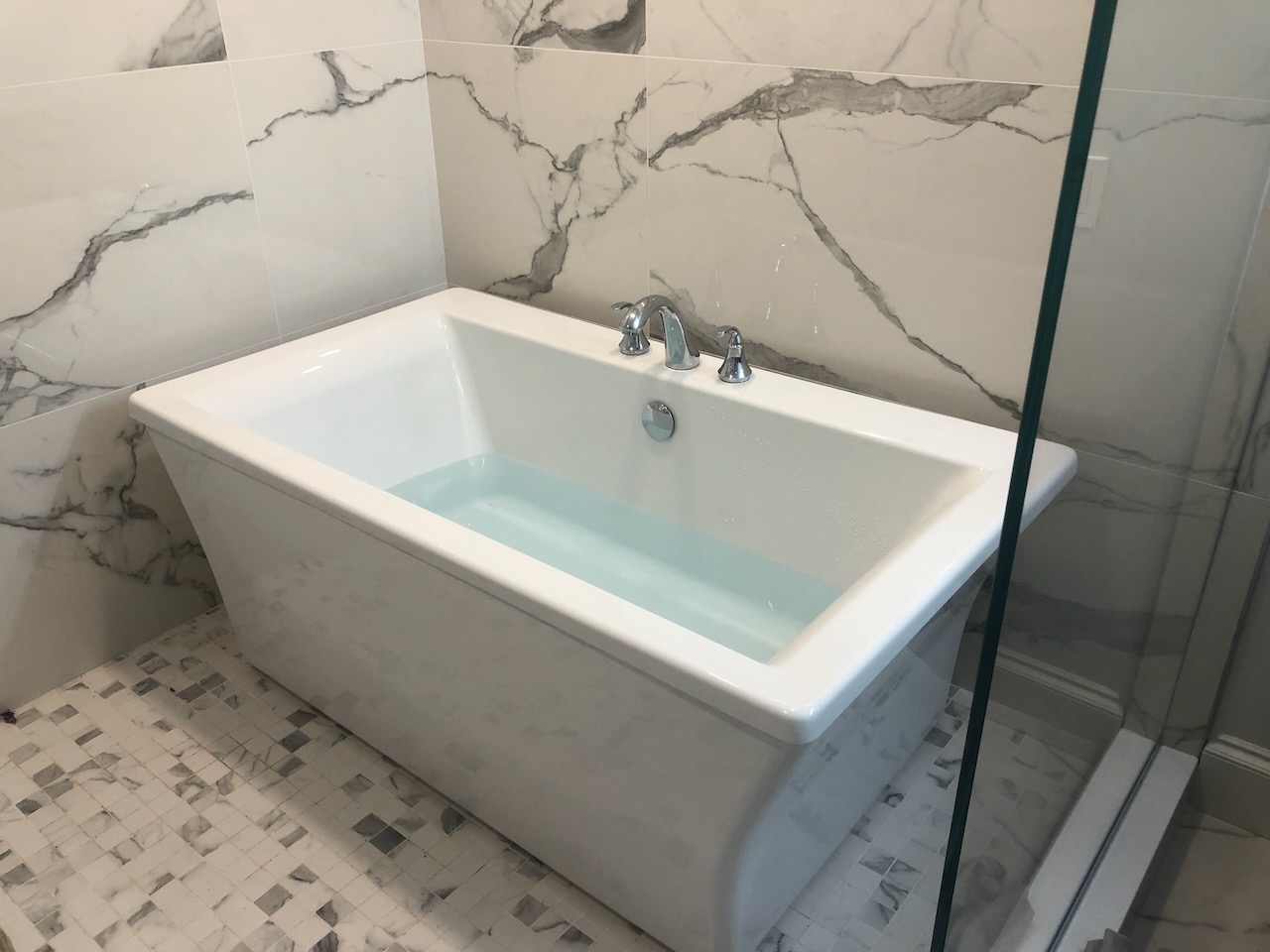 Freestanding soaking tub with marble walls and tiled shower floor in Ridgewood, NJ by Fairmount Heights Homes.