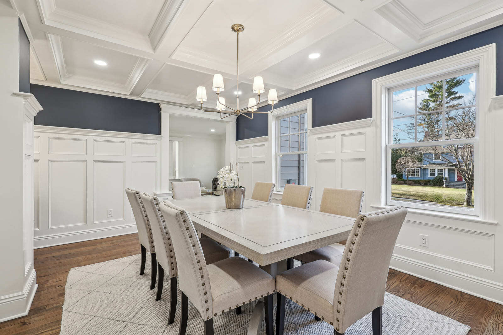 Formal dining room in Ridgewood, NJ with coffered ceiling, navy walls, and upholstered chairs